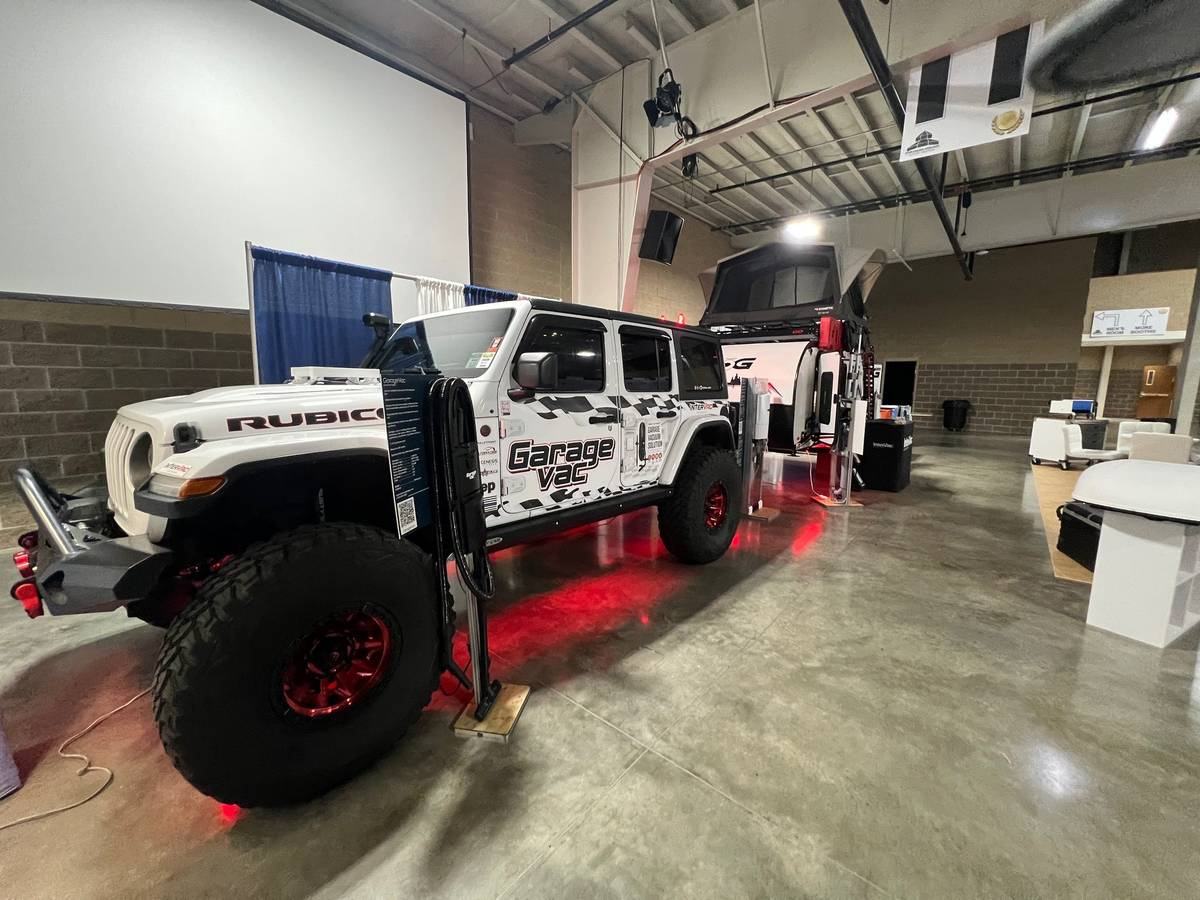 The InterVac show vehicle, a white Jeep Wrangler Rubicon in GarageVac livery with red underglow, displayed on polished concrete at a trade show alongside a GarageVac demo stand.