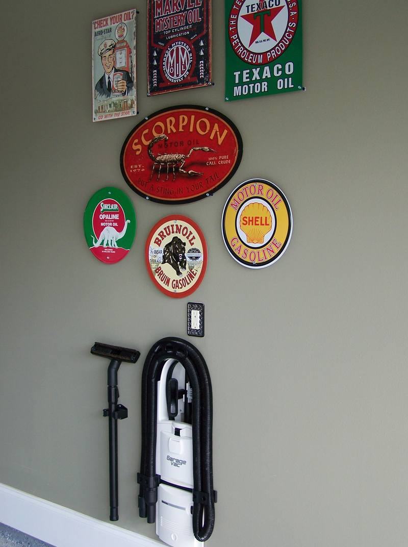 A white GarageVac mounted low on a garage wall beneath a collection of vintage Texaco, Shell and Sinclair motor-oil signs.